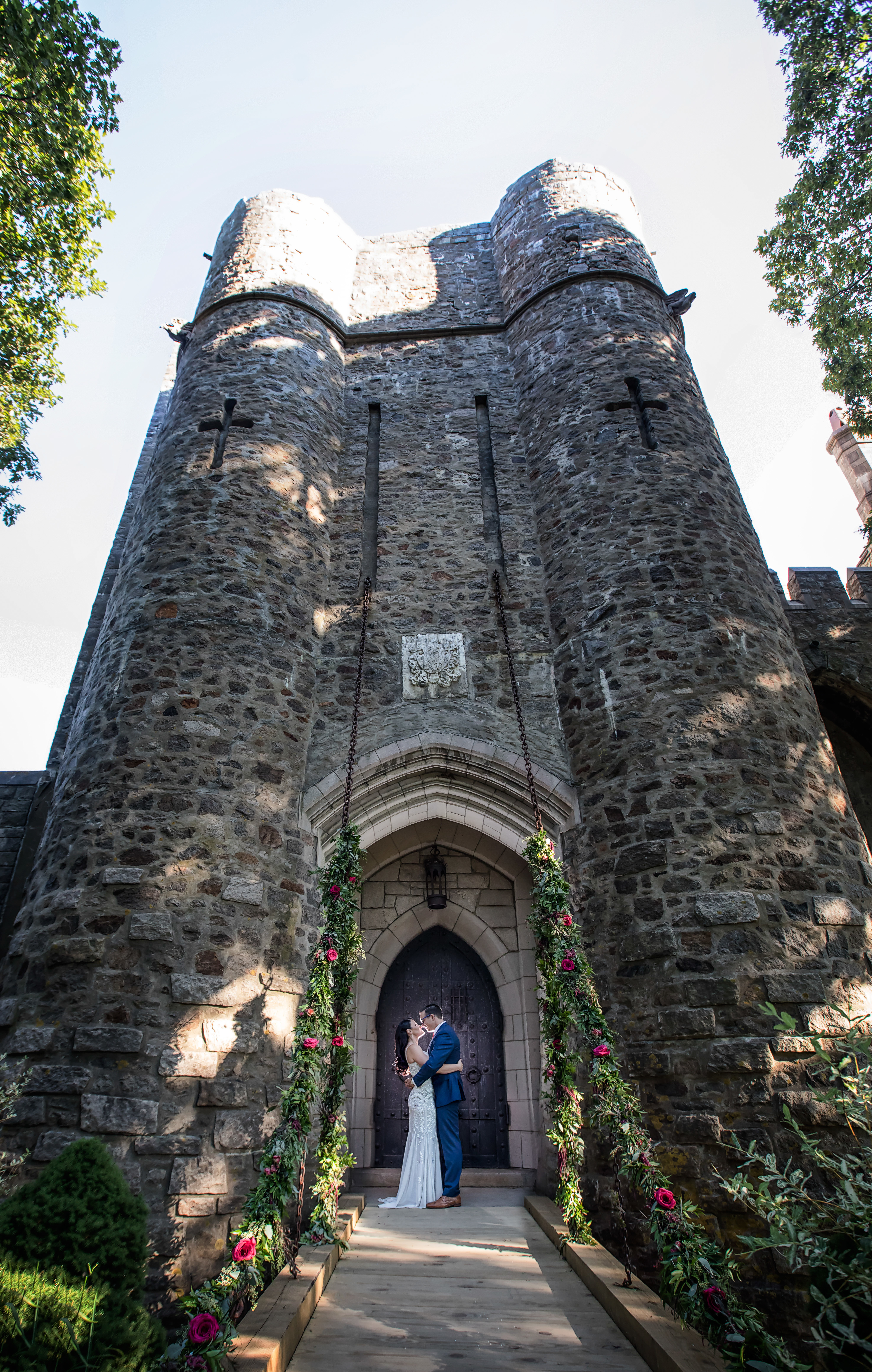 Bride and Groom photographed at Hammond Castle Museum. Wedding flower garlands go up the chains of the drawbridge. Dark and moody wedding photos. Wedding Inspiration at Hammond Castle.