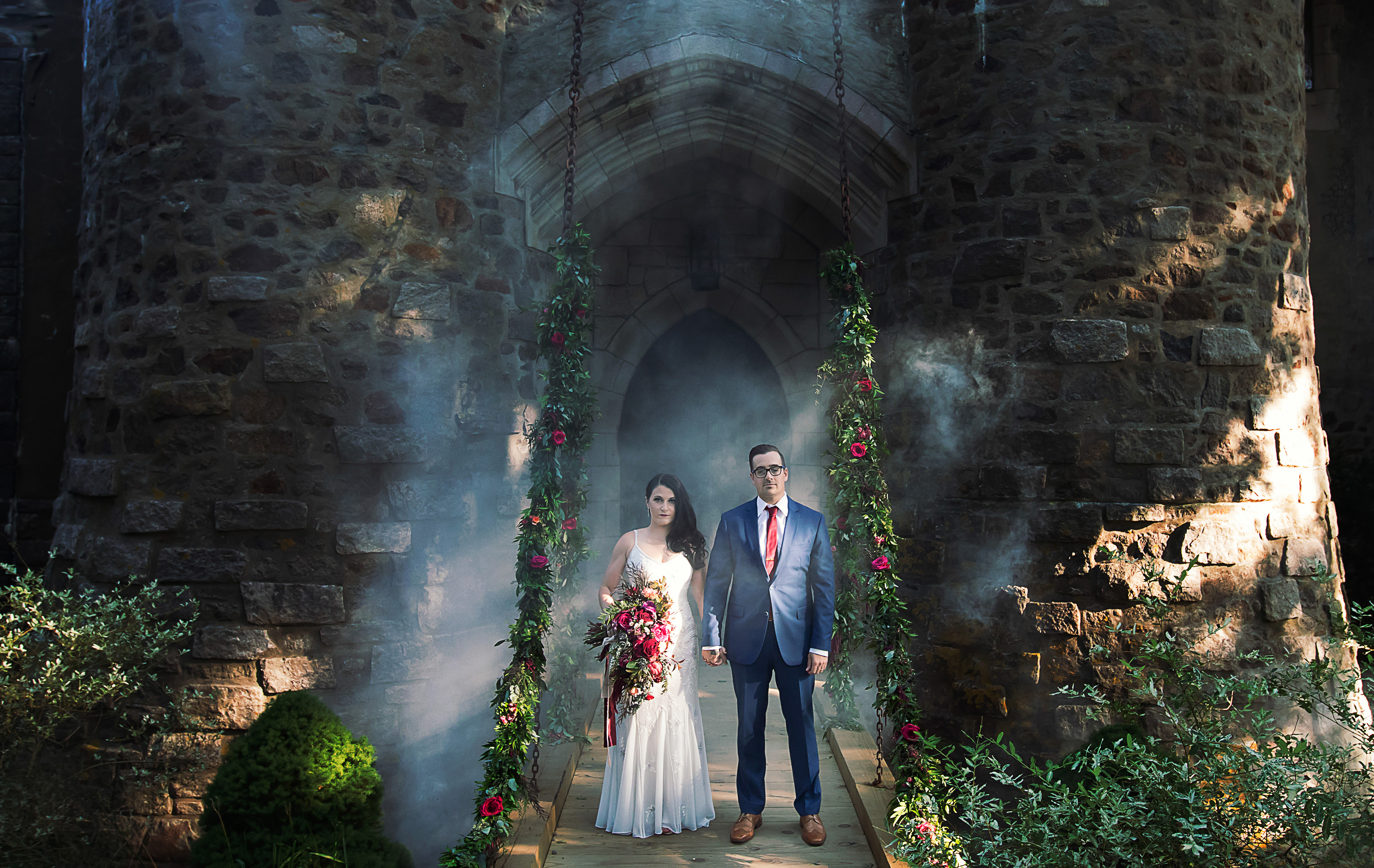 Wedding couple being photographed at Hammond Castle Museum. Bride and Groom wedding Portrait. Floral garlands adorn the drawbridge chains.